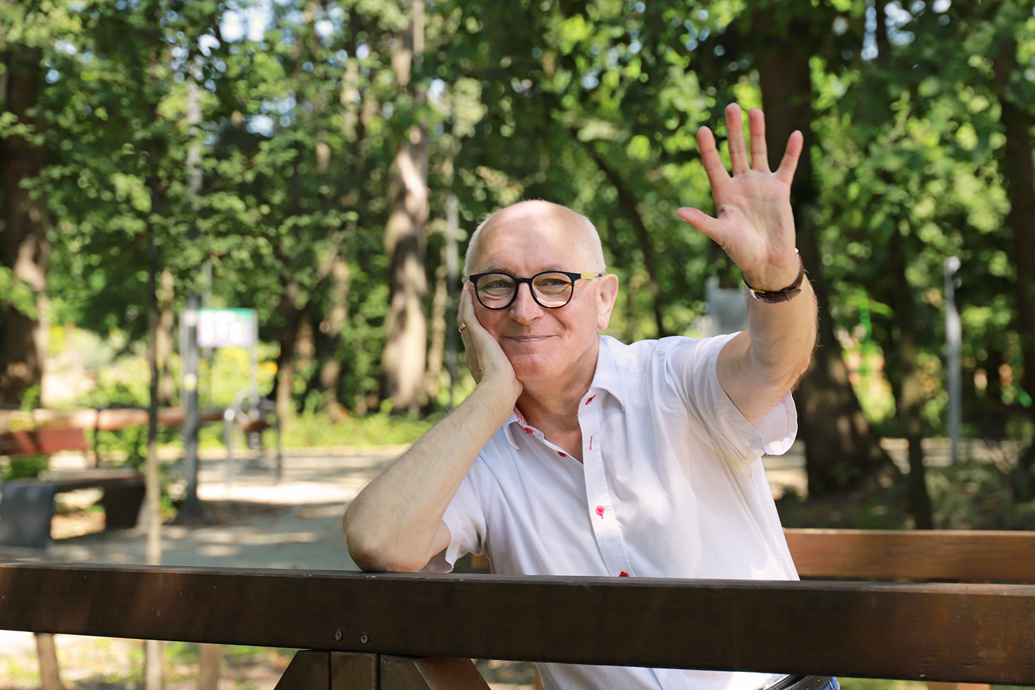 Natural Pharmaceuticals ImuBerin Egy középkorú férfi fehér ingben és szemüvegben mosolyogva integet.